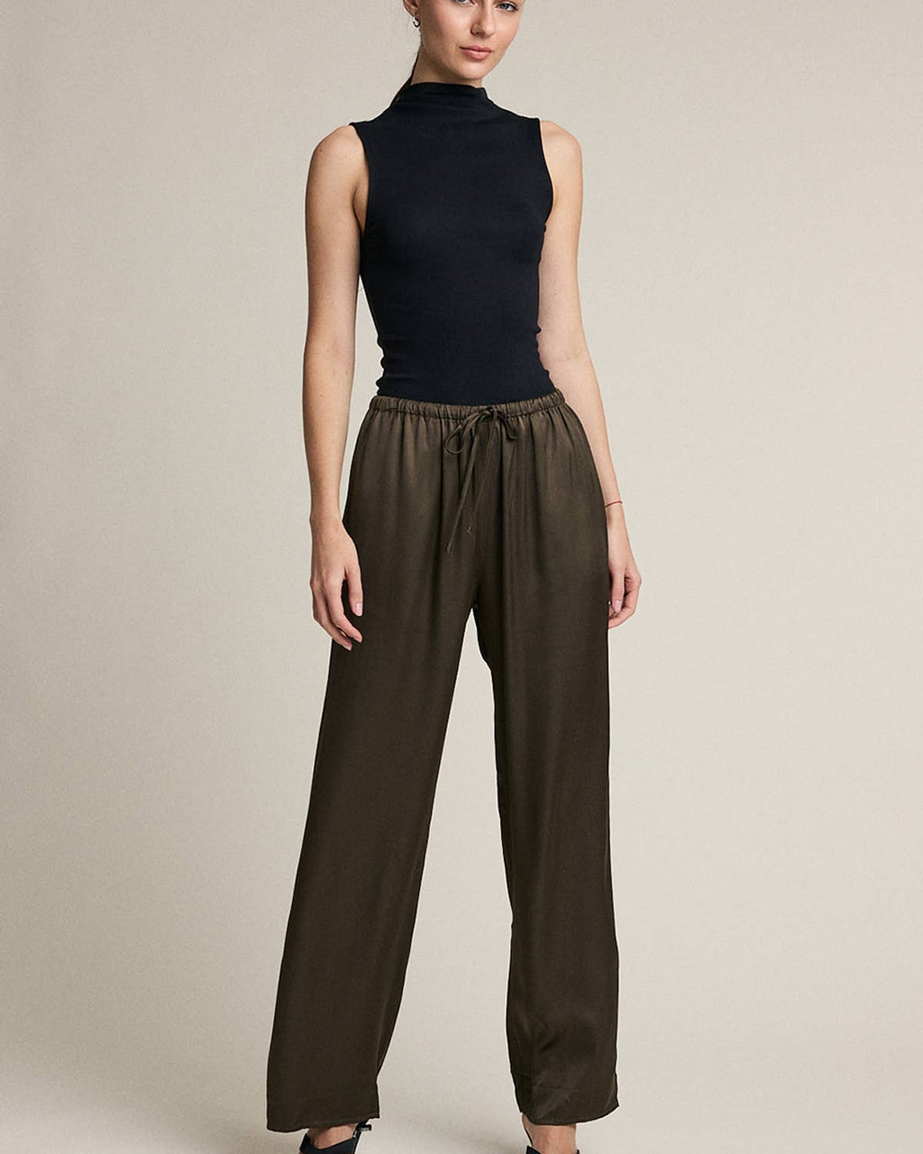 Woman wearing a black sleeveless top and brown wide-leg pants on a beige background